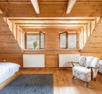 Attic room with wooden paneling, two beds, and an armchair, floor with wooden decor.