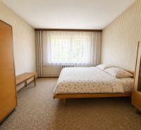 A bedroom in a two-room apartment with simple furniture and patterned wallpaper.