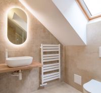 A bathroom with an oval mirror, sink, radiator, and slanted ceiling.