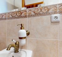Sink faucet and bathroom tiles in a family house with a decorative pattern.