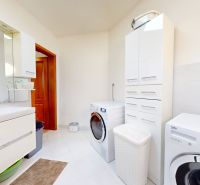 Bathroom with a washing machine, white cabinets, and a sink in a family house.