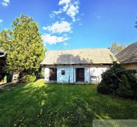 A cottage in Šahy with a shingle roof, a large garden, and trees.