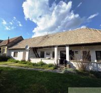 A cottage in Šahy with a large roof and a white facade in the countryside.