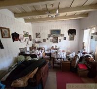 Room in a cottage with many antiques, paintings, and a wooden beam ceiling.