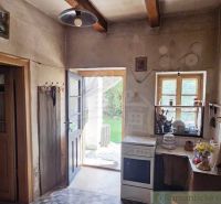 Rustic kitchen in a cottage with wooden beams, a stove, and a view of the garden.