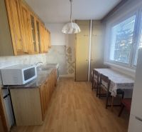 A kitchen unit with upper cabinets, a microwave, and a wooden decor floor in a 3-room apartment.