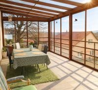 A glass-enclosed veranda in a family house with a dining table and a view.