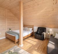 Attic room with a bed, chair, and wooden decor flooring in a family house.