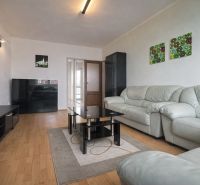 Living room with wood-patterned flooring, a sofa, and paintings, in a three-room apartment.