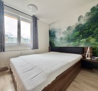 A bedroom with a bed, a forest photo wallpaper, and a wooden decor floor in a three-room apartment.