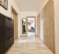 A hallway in a 3-room apartment with a wooden decor floor and a mirror.