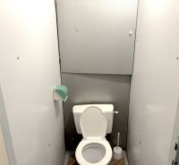 A bathroom in a studio apartment with white walls and a floor with a wood design.