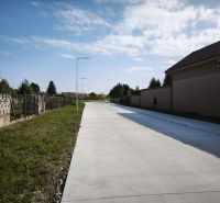 Concrete sidewalk in Čierny Brod for residential plots next to grassy and fenced areas.