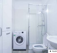A bathroom in a studio apartment with a washing machine, shower, and sink in white tones.