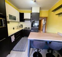 A kitchen in a 3-room apartment with black cabinets and a floor with a wood design.