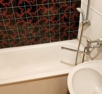 A bathroom in a studio apartment with a bathtub and a sink, dark patterned tiles.