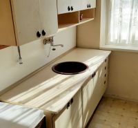 A kitchen in a one-room apartment with a simple kitchenette, built-in sink, and a window.