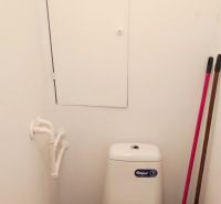 Toilet with storage space above the tank in a studio apartment, floor with wooden decor.