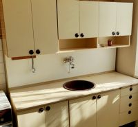 A kitchen in a studio apartment with tiles and light-colored furniture.