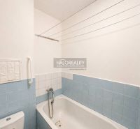 A bathroom with a bathtub and light blue tiles in a studio apartment.