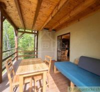 The veranda of a family house in Cinobana with seating and a wooden table by the forest.