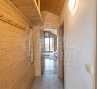 A narrow hallway with wooden paneling and a view into the living room of a family house.