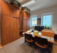 Offices with wooden furniture, documents on the table, two windows, and hanging ceiling lights.