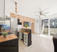 A kitchen in a 2-room apartment with a wooden decor floor and a brick wall.