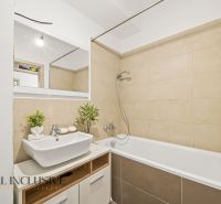 A bathroom with light tiles, a shower over the bathtub, and a sink in a 2-room apartment.