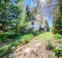 A cottage in Nitra surrounded by trees and a green lawn under a clear blue sky.