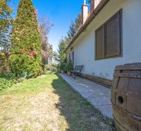 The exterior of the cottage in Nitra with a lawn, trees, and a barrel.