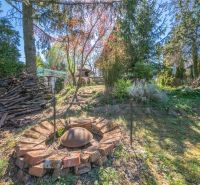 A garden with a fire pit next to a cottage in Nitra surrounded by trees and wood.