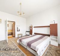 Bedroom in a family house with a double bed, striking carpets, and a wooden-patterned floor.