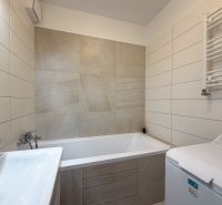 A bathroom in a 2-room apartment with a bathtub, sink, and washing machine, tiled with light tiles.