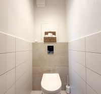 A toilet in a 2-room apartment with white tiles and storage space.