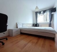 A bedroom in a two-room apartment with a wooden decor floor, a bed, and a chair.