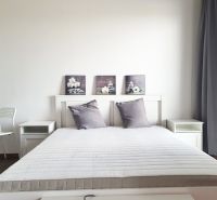 Bright bedroom with a white bed, wall decorations, and a wood-patterned floor.
