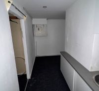 A narrow interior of commercial premises with a sink and neutral walls.