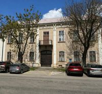 A building in Komárno used for special properties, surrounded by trees and a parking lot.