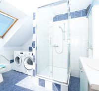 Bathroom in a family house with tiled floor, shower corner, and washing machine.