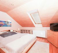 Attic bedroom with a bed, television, and wood-patterned flooring in a family house.