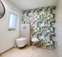 Bathroom in a family house with leaf-patterned tiles and a wall-mounted toilet.