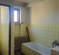 A bathroom in a family house with a bathtub, light tiles, and two windows.