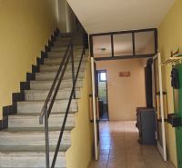 Interior of a family house with a tiled stove, staircase, and wall-mounted coat rack.