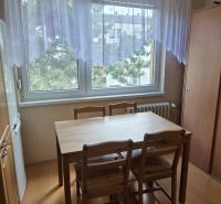 Dining area with a table and chairs, floor with wood decor, curtain on the window.