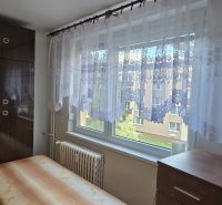 A room in a one-bedroom apartment with a wooden wardrobe, a bed, and curtains on the window.