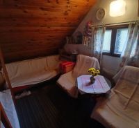 A room with a slanted ceiling, armchairs, a table with a tablecloth and flowers, wooden paneling.