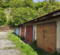 Row garages on Dlhá Street in Prievidza, with greenery and trees in the background.