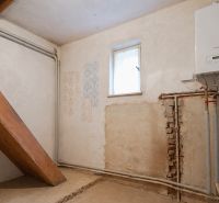 Boiler room with a boiler and piping in a family house, with a small window.