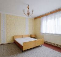 A bedroom with wallpaper, wooden furniture, and a large window in a family house.